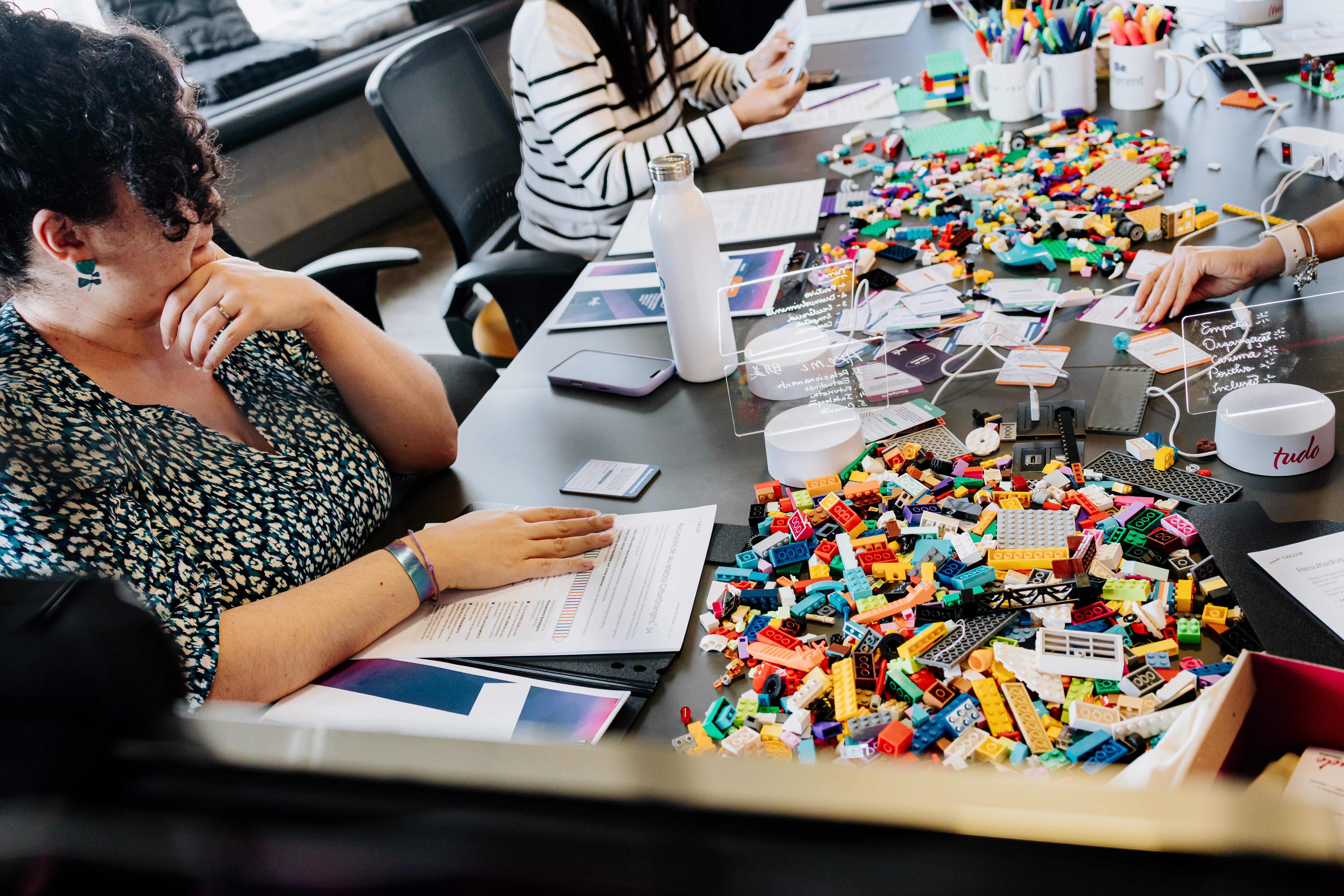 Tela exibindo o slide 'Quem sou eu no time?' durante atividade individual do workshop de liderança da Basepex, com participantes construindo com peças de LEGO® sobre a mesa.